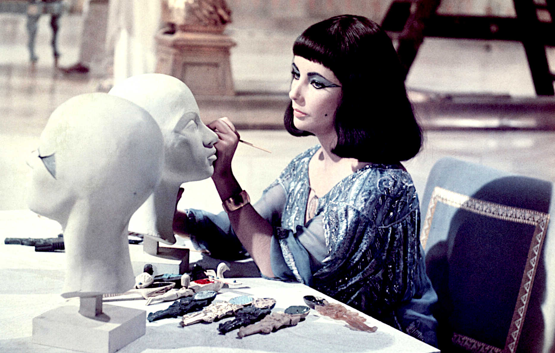 The beautiful Elizabeth Taylor on set applying makeup to clay face models in 1963